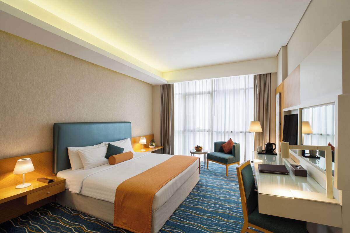 Une chambre d’hôtel avec un lit, un bureau, une chaise et une grande fenêtre avec des rideaux.