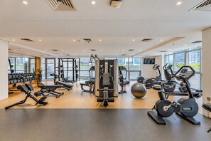 Une salle de sport moderne, dotée de divers appareils d’exercice, de grandes fenêtres et d’un aménagement propre et bien organisé.