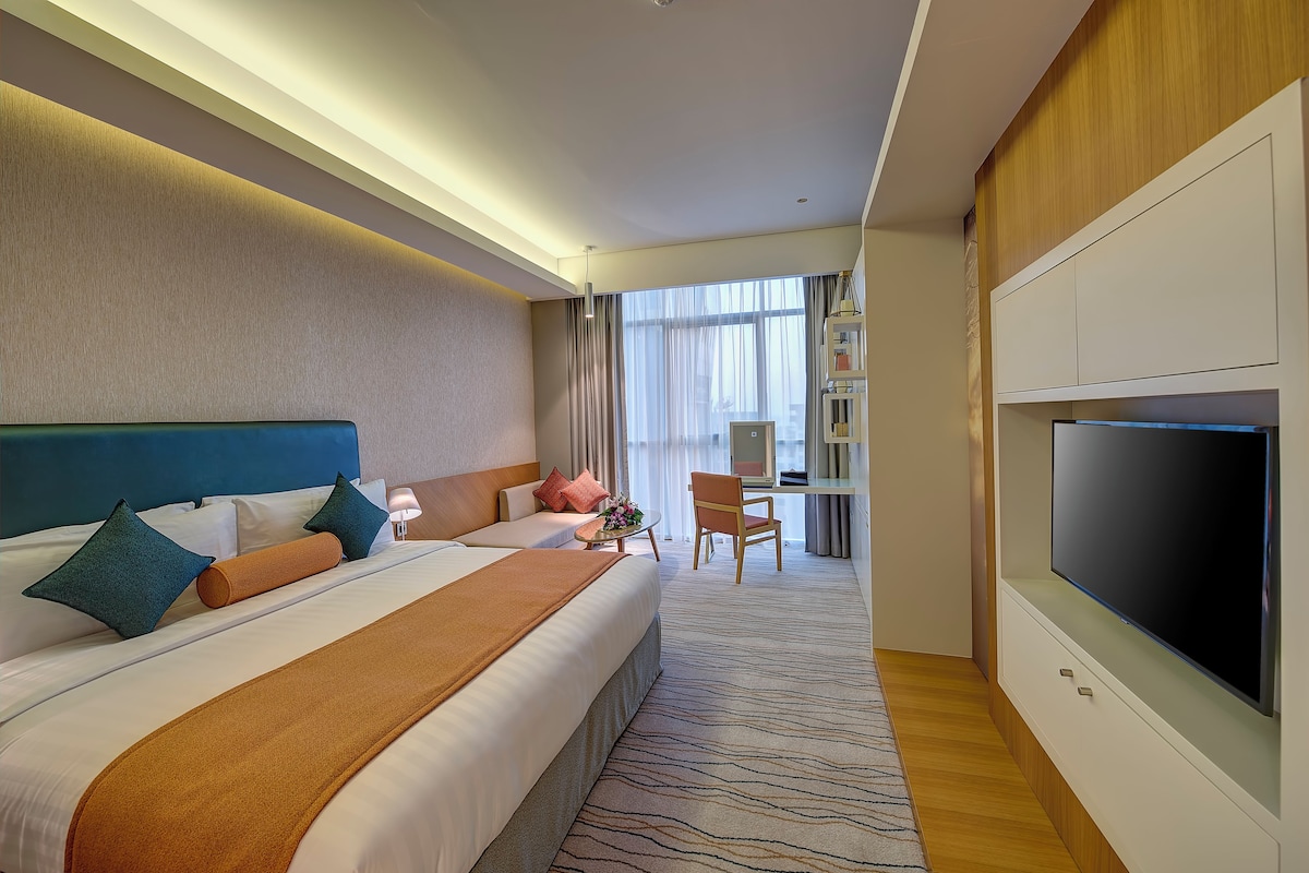 Una habitación de hotel con una cama grande, televisión, escritorio y silla.