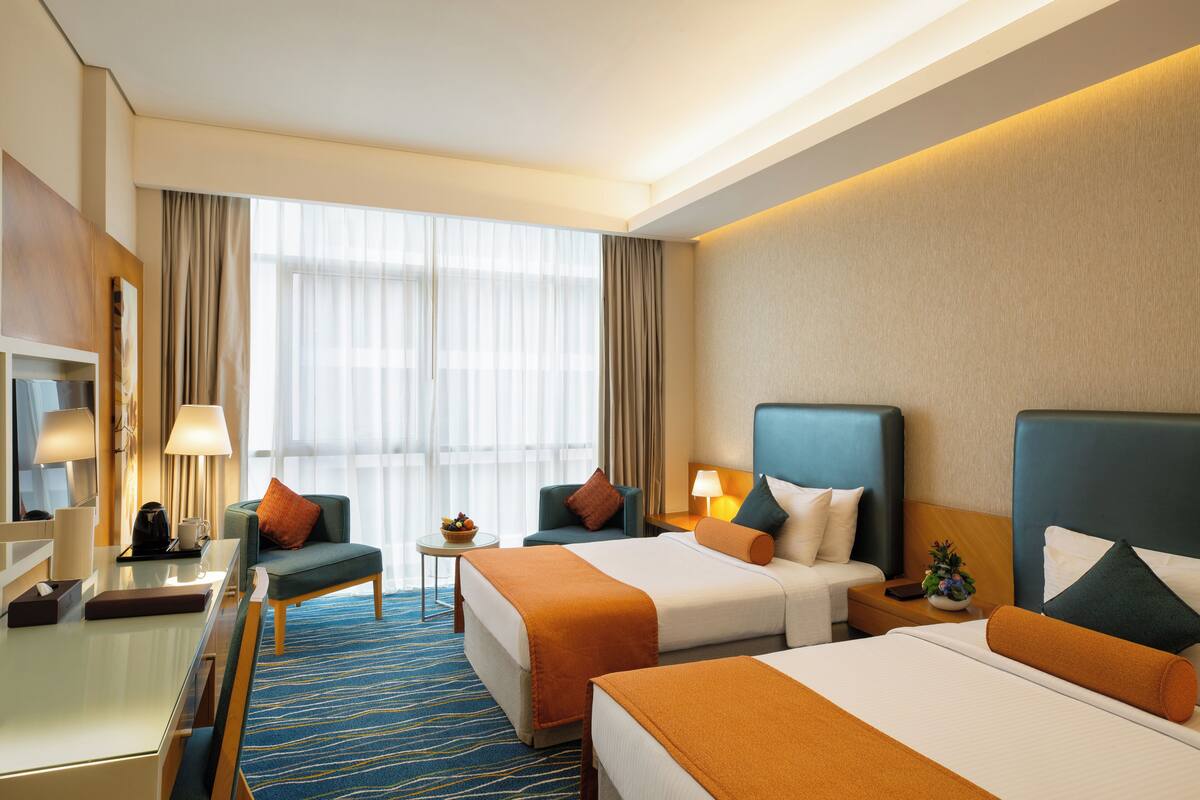 Une chambre d’hôtel avec deux lits, un bureau, une chaise et une petite table avec une lampe.