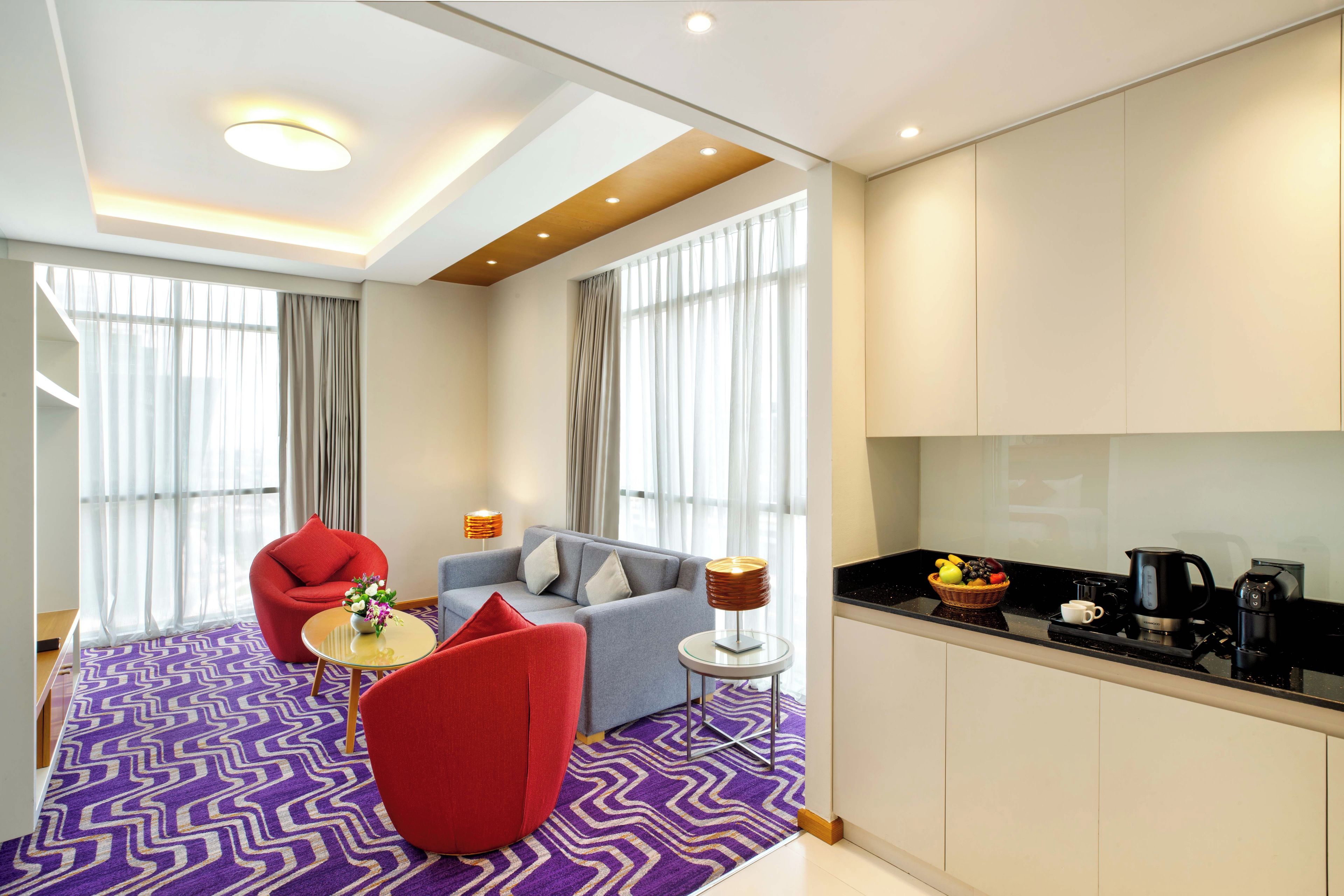 Ein modernes Hotelzimmer mit einer Couch, einem Sessel und einem kleinen Tisch mit Lampe und Blumen.