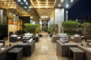 Un moderno vestíbulo de hotel con mobiliario de mimbre, suelo de mármol y un cartel con el nombre del hotel.