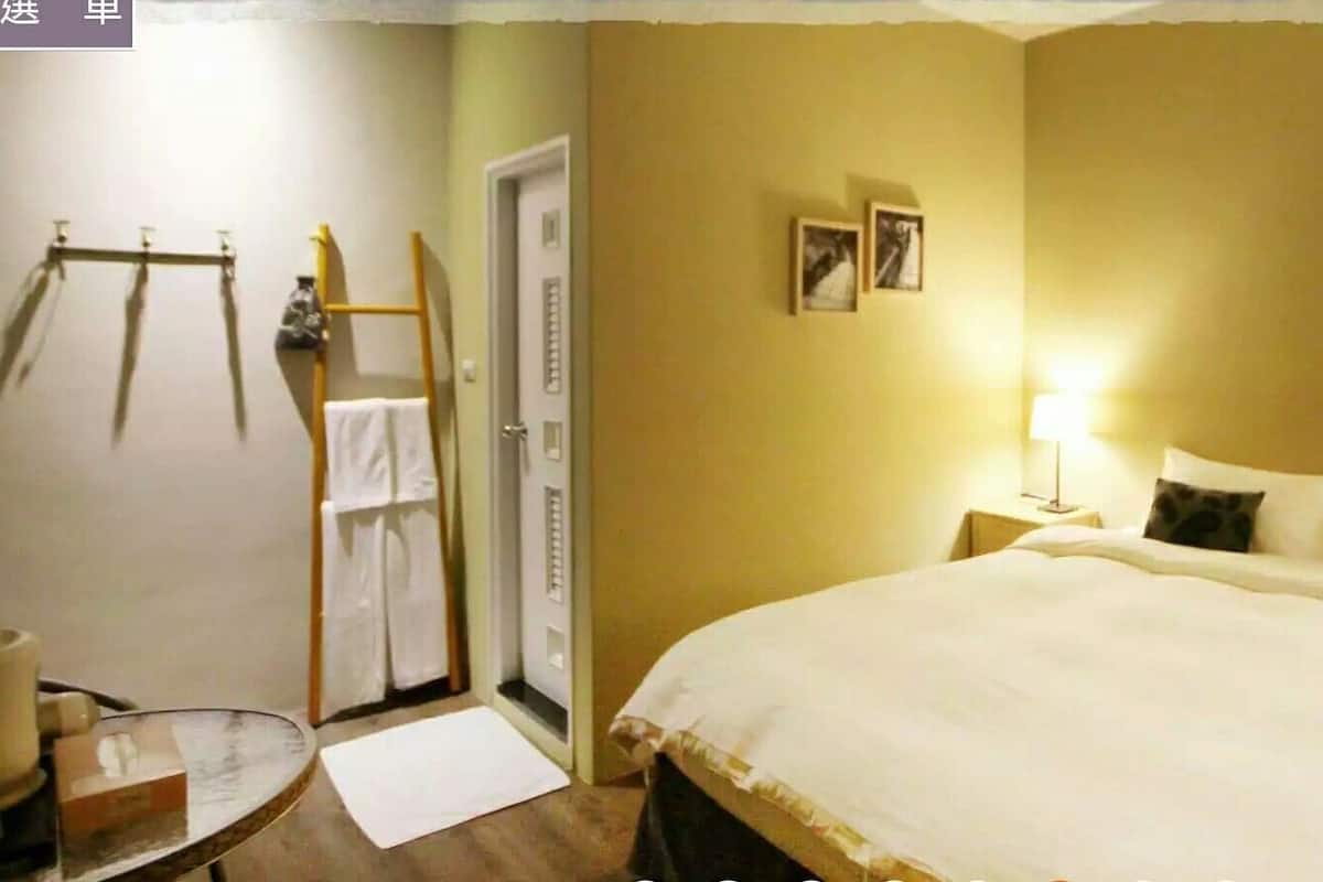 Ein Hotelzimmer mit einem großen Bett, Nachttischlampen, einem kleinen Tisch und einer Tür mit Handtuchhalter.