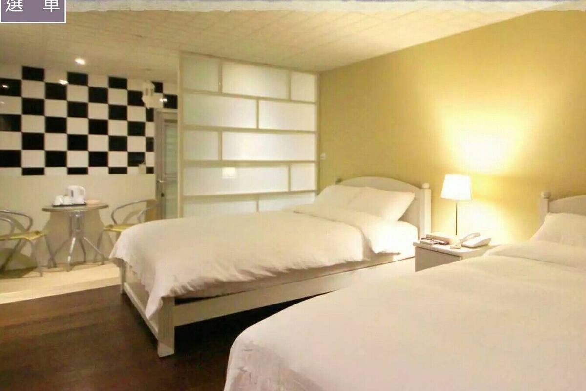 Ein Hotelzimmer mit zwei Betten, einer karierten Wand, einem kleinen Tisch und einer Lampe.