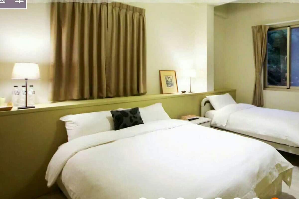 Ein Hotelzimmer mit zwei Einzelbetten, einem Nachttisch mit Lampe, einem Fenster mit Vorhängen und einer Klimaanlage.
