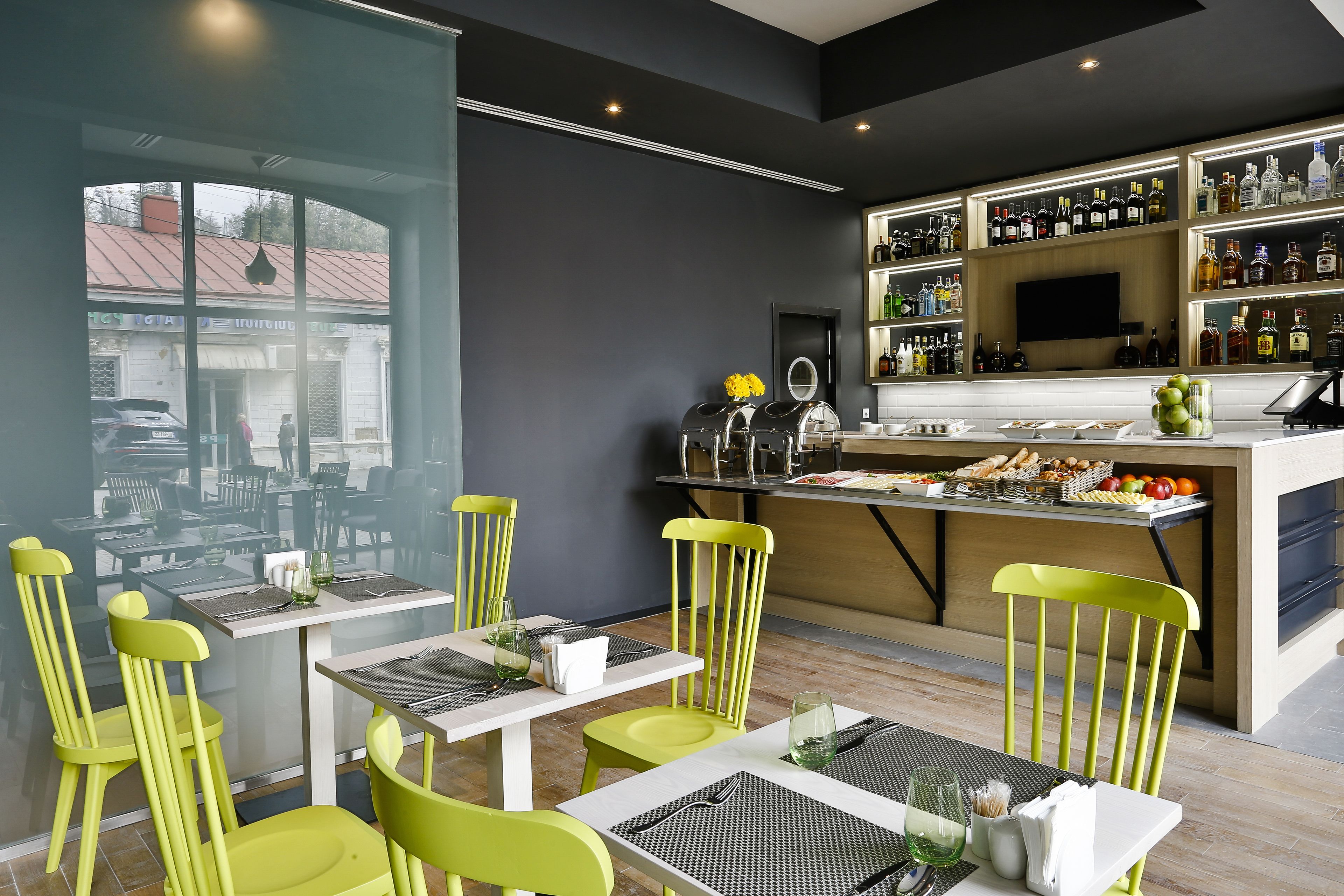 A restaurant with a bar area, tables with chairs, and a view of the street outside.