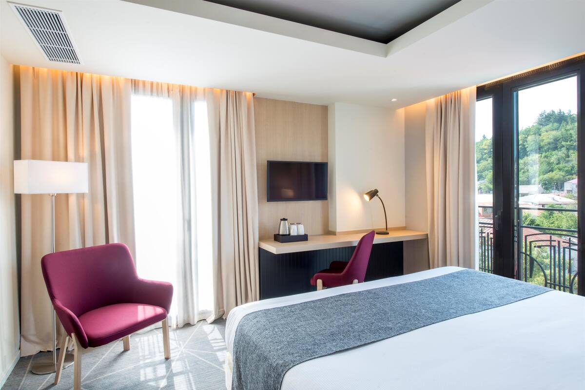 A modern hotel room with a bed, a desk, a chair, and a TV.