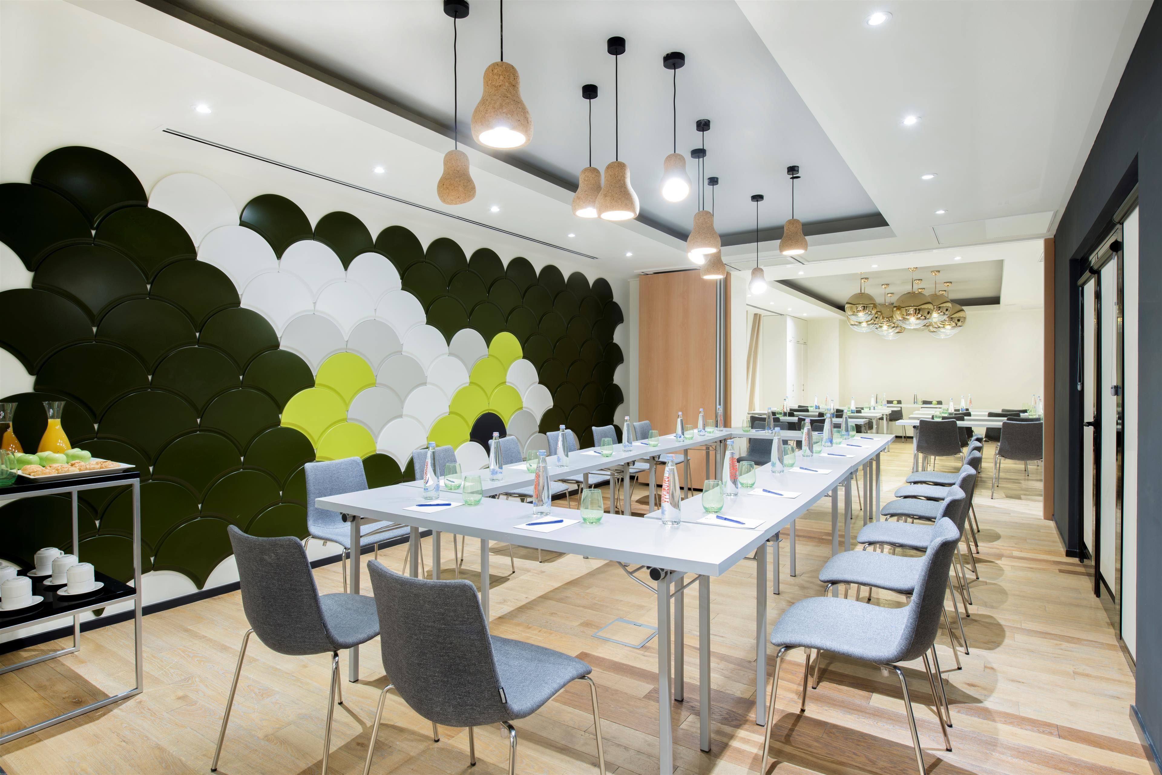 A modern conference room with white tables, grey chairs, and a decorative wall with green and white panels.