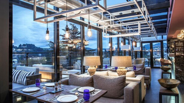 Comedor moderno con vistas a la ciudad, que presenta techo de cristal, mobiliario contemporáneo e iluminación ambiental.