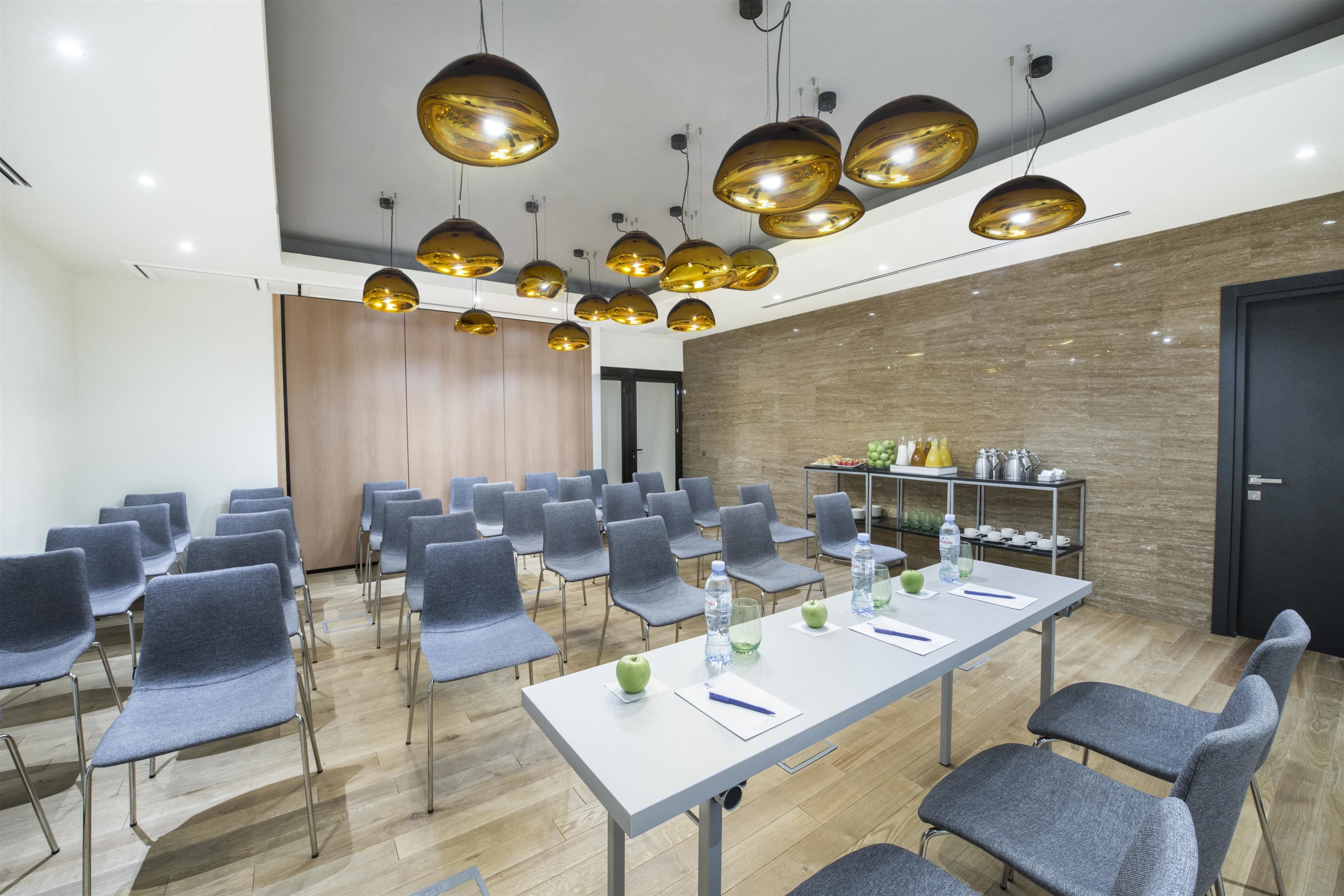 A conference room with rows of chairs, a long table with water bottles and apples, and a kitchen area with various appliances.