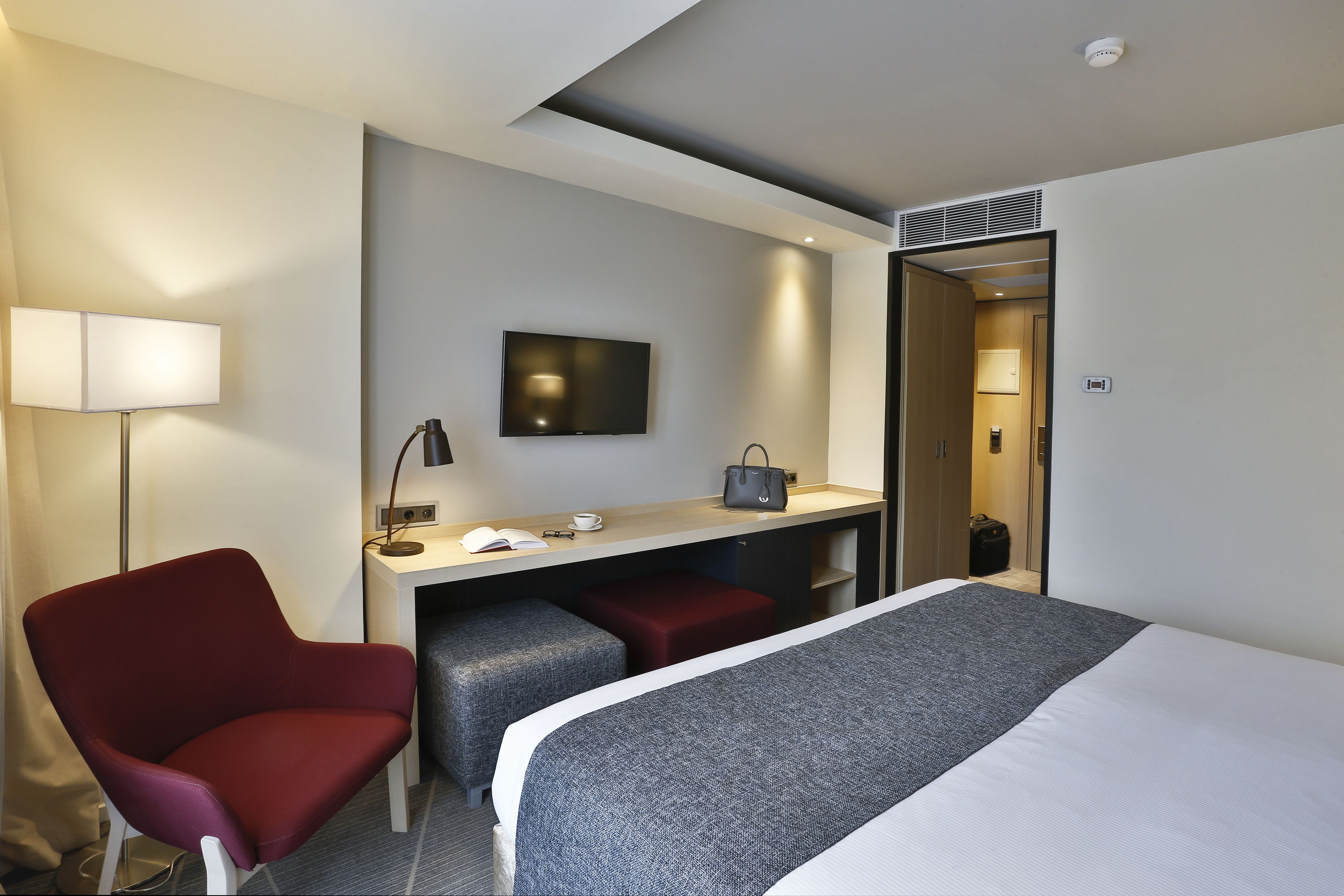Una habitación de hotel con una cama, un escritorio con una silla, un televisor y una lámpara.