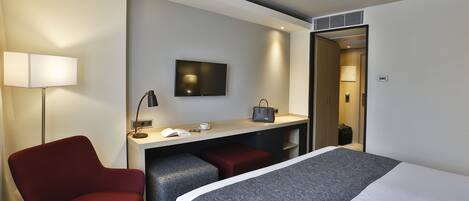 Una habitación de hotel con una cama, un escritorio con una silla, un televisor y una lámpara.