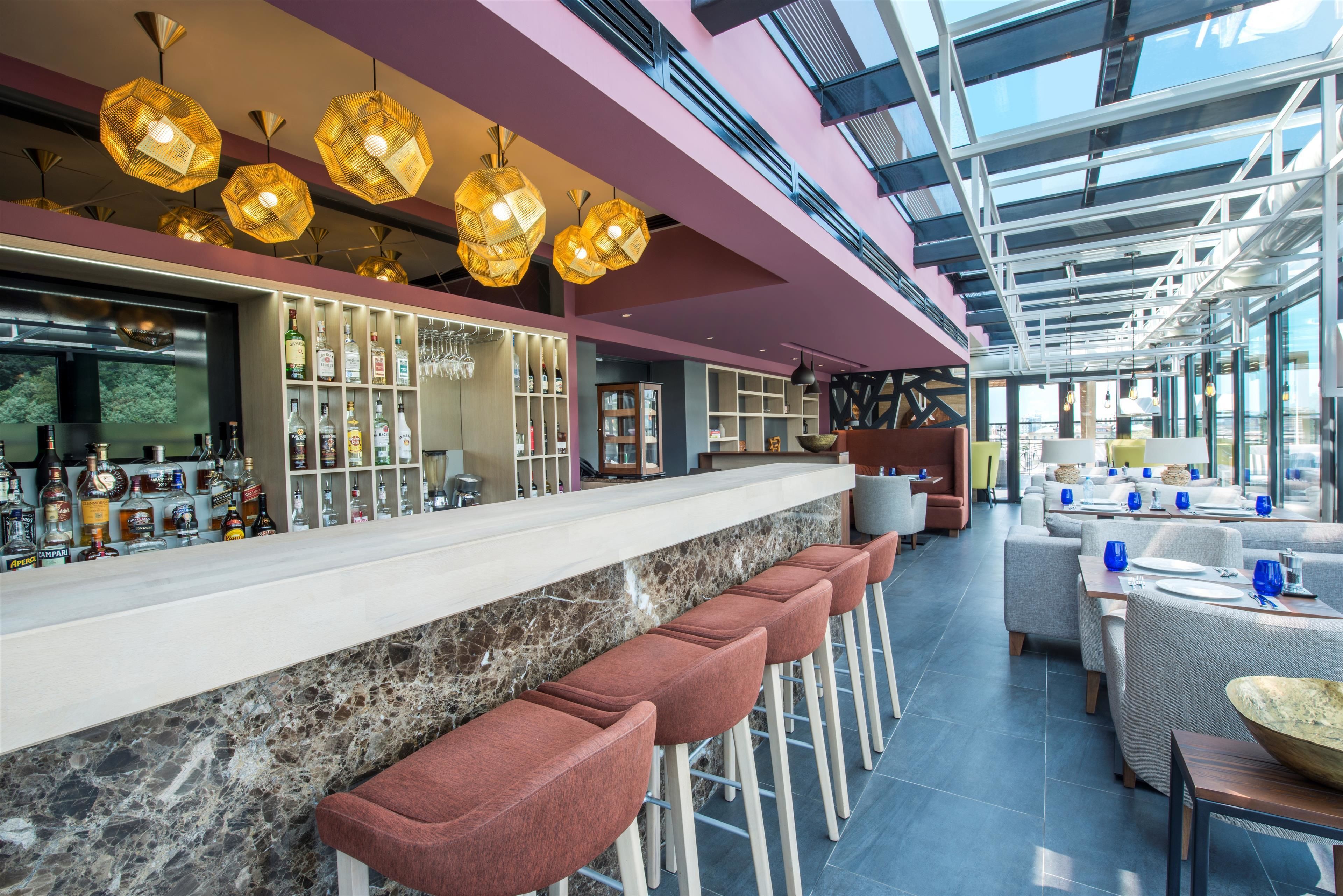 Un área de bar moderna con una barra larga, varios taburetes y una gran variedad de botellas.