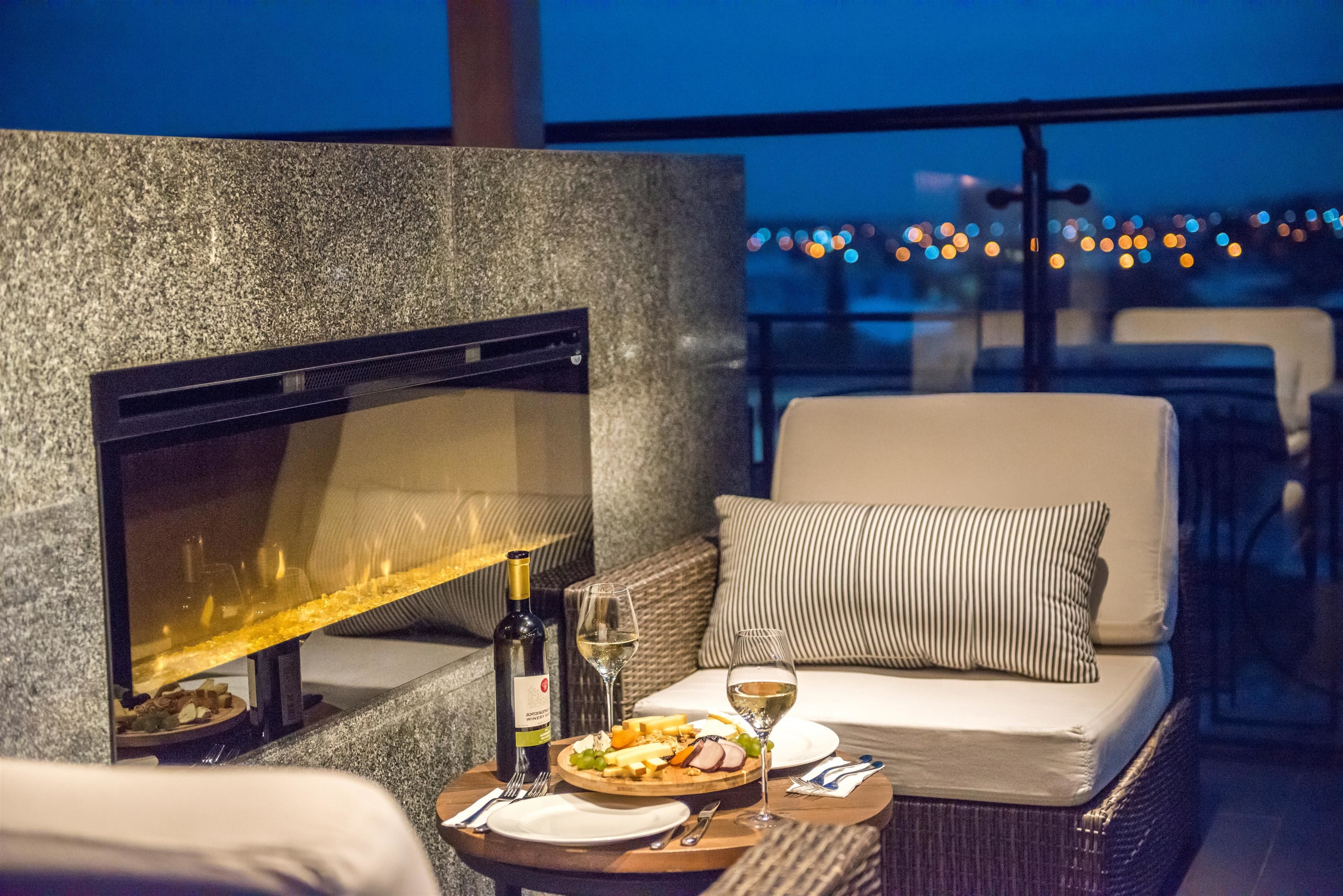 A cozy outdoor seating area with a fireplace, a dining table with plates, glasses, and a bottle of wine.