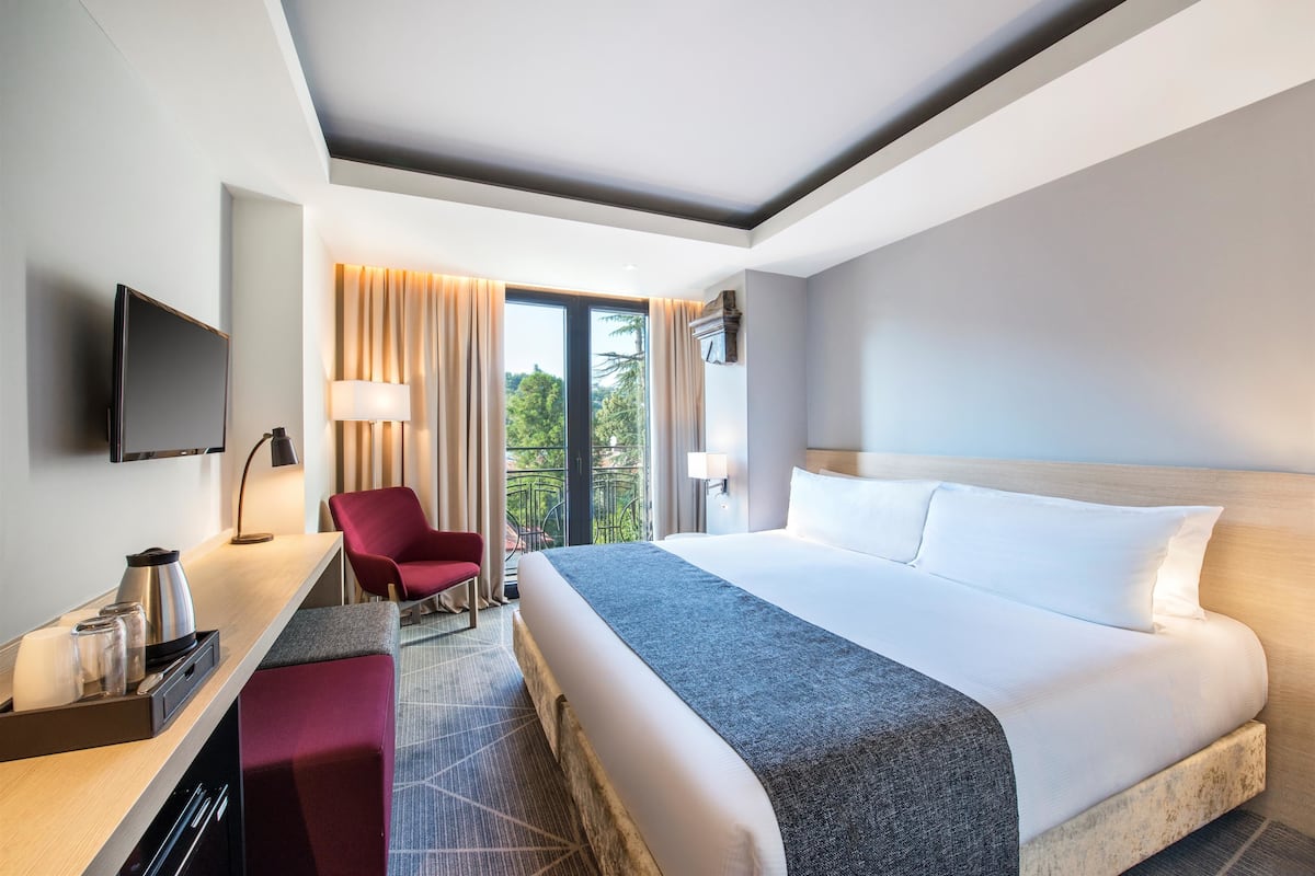 A hotel room with a large bed, a desk with a coffee maker, a TV, and a red chair.