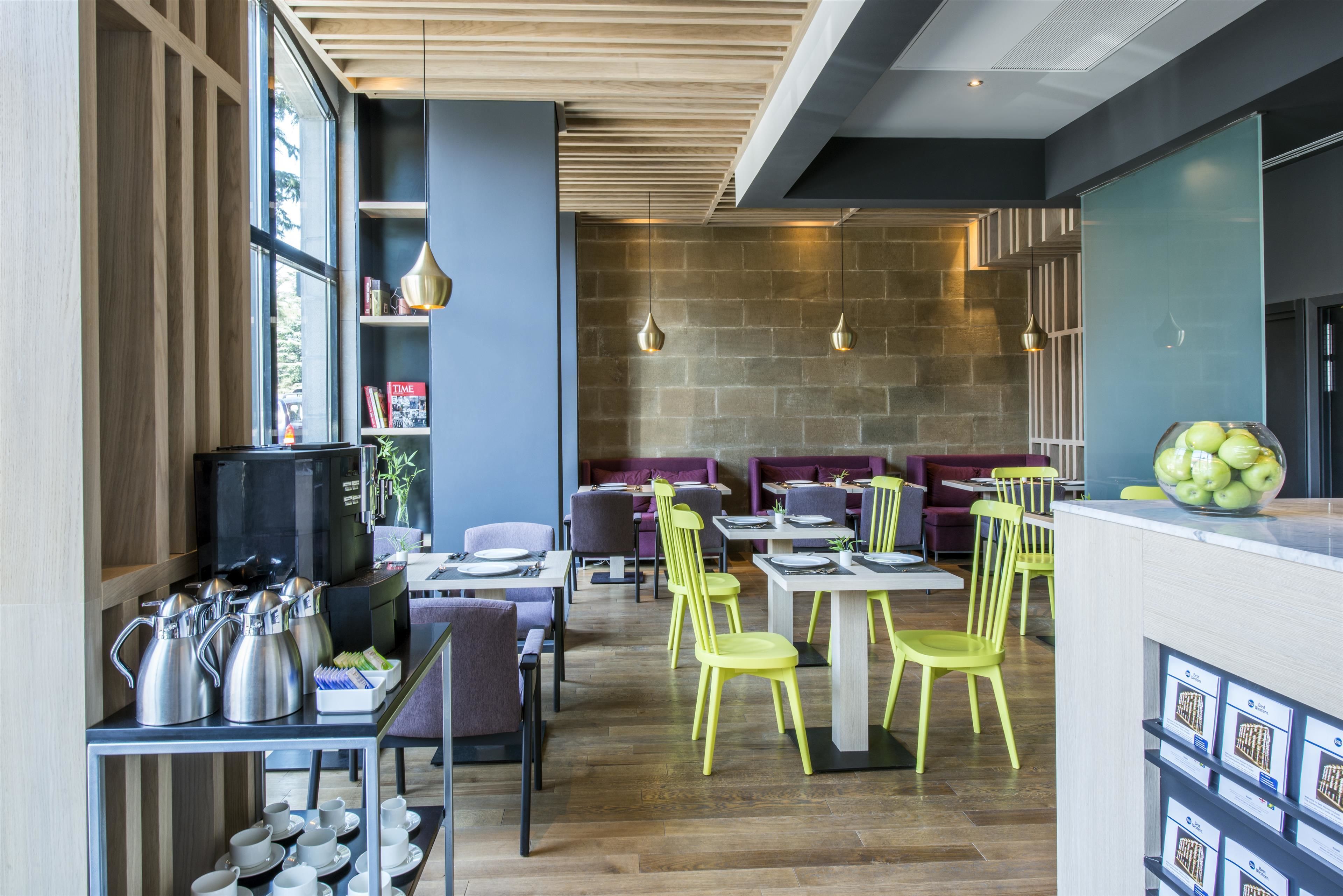 A modern restaurant with wooden floors, yellow chairs, and a stone wall.