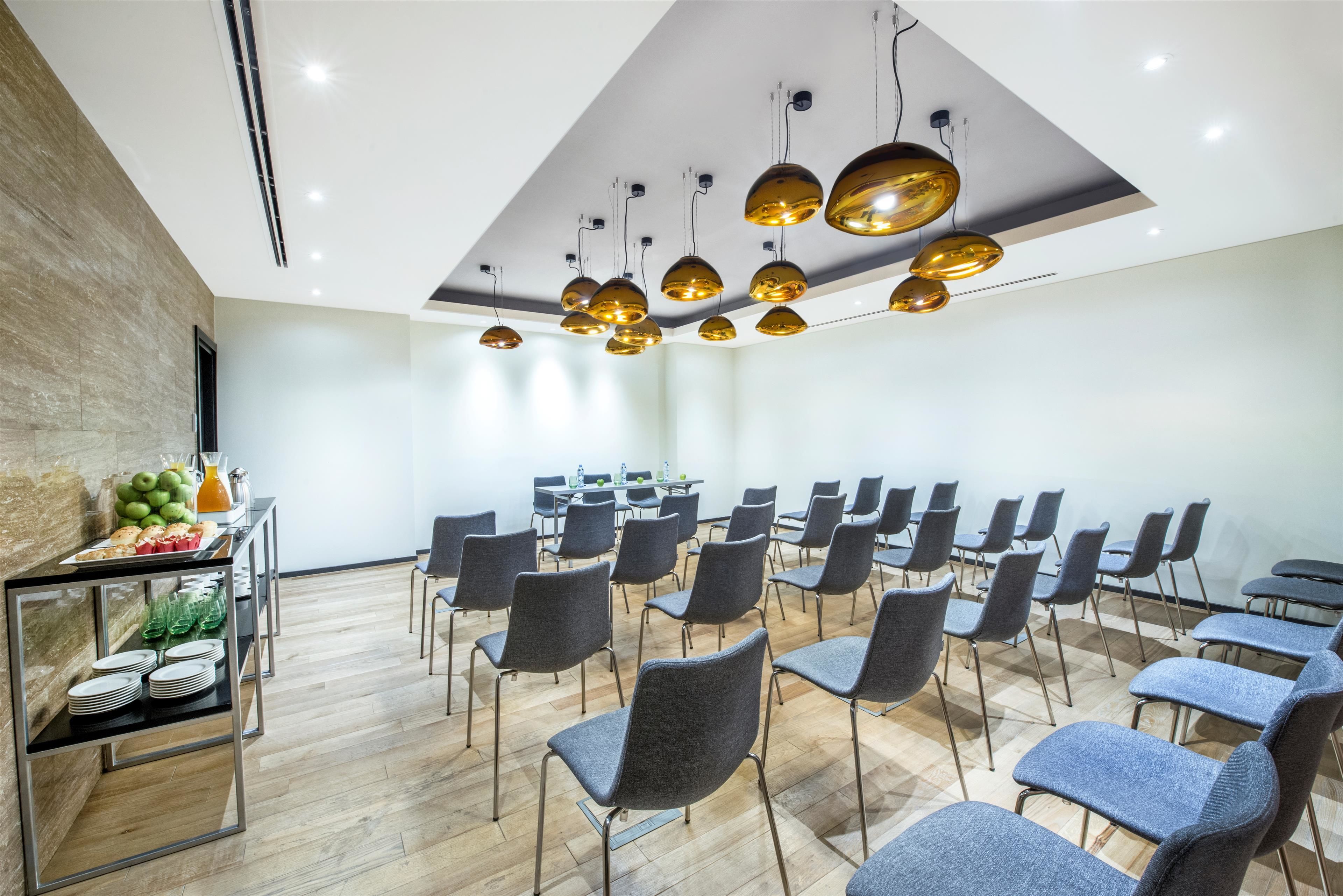 A conference room with a modern design, featuring a wooden floor, grey chairs, and a ceiling with hanging pendant lights.