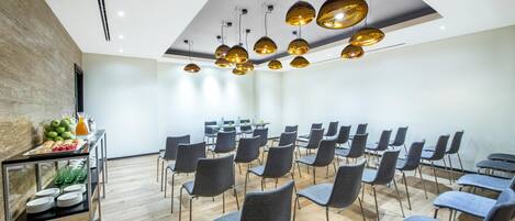 A conference room with a modern design, featuring a wooden floor, grey chairs, and a ceiling with hanging pendant lights.
