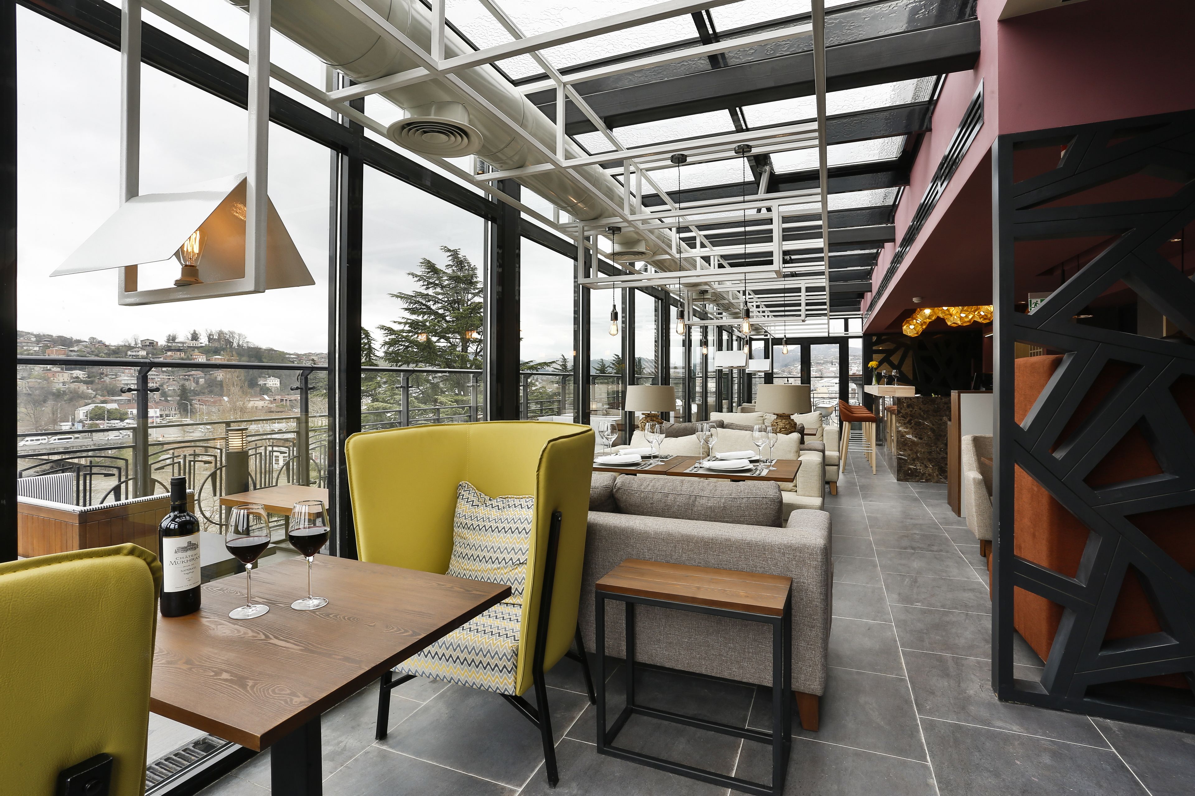 A modern restaurant with a terrace, large windows, and a view of the city.