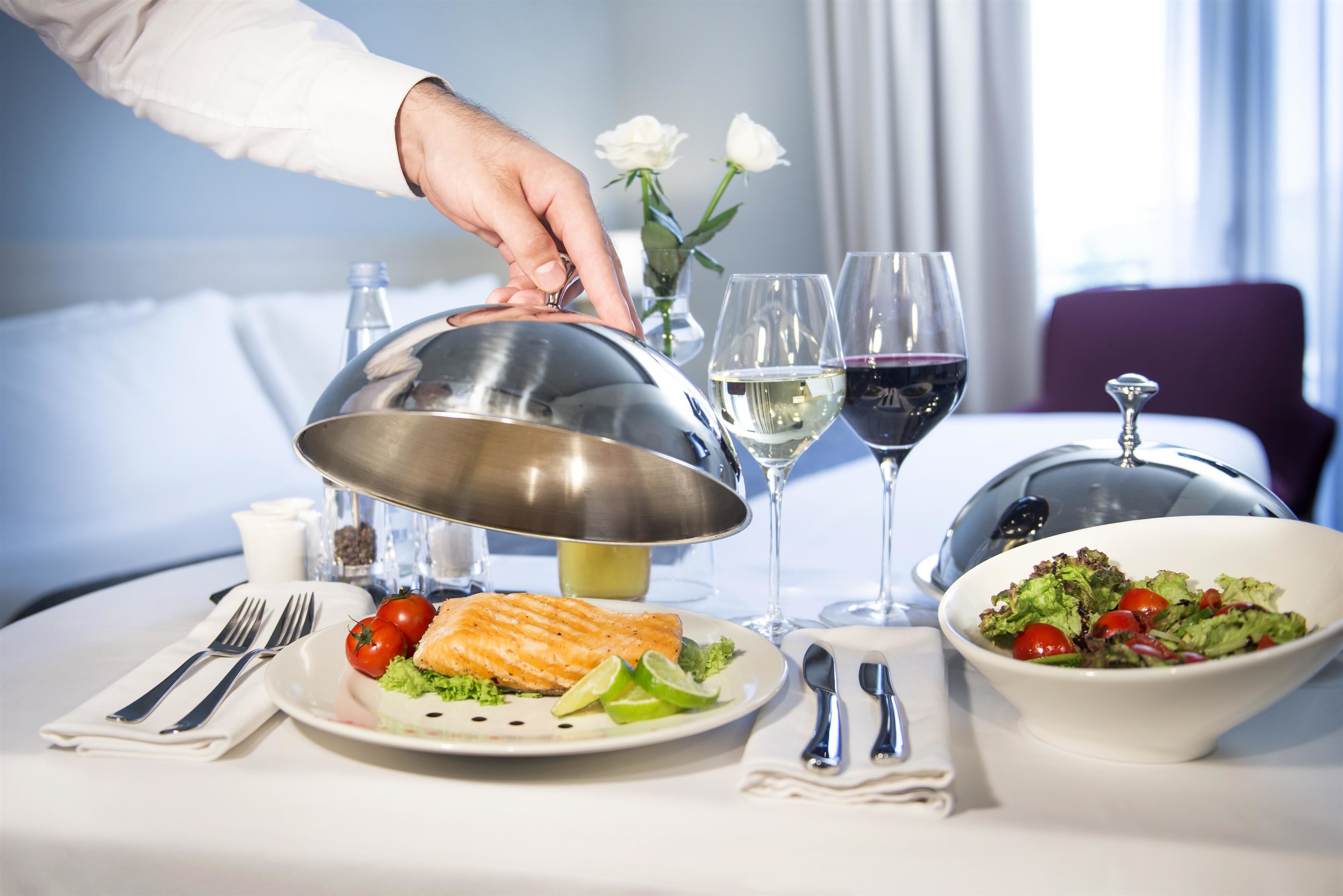 Ein Esstisch ist gedeckt mit Lachs auf einem Teller, einer Salatschüssel, Weingläsern und einer Wasserflasche.