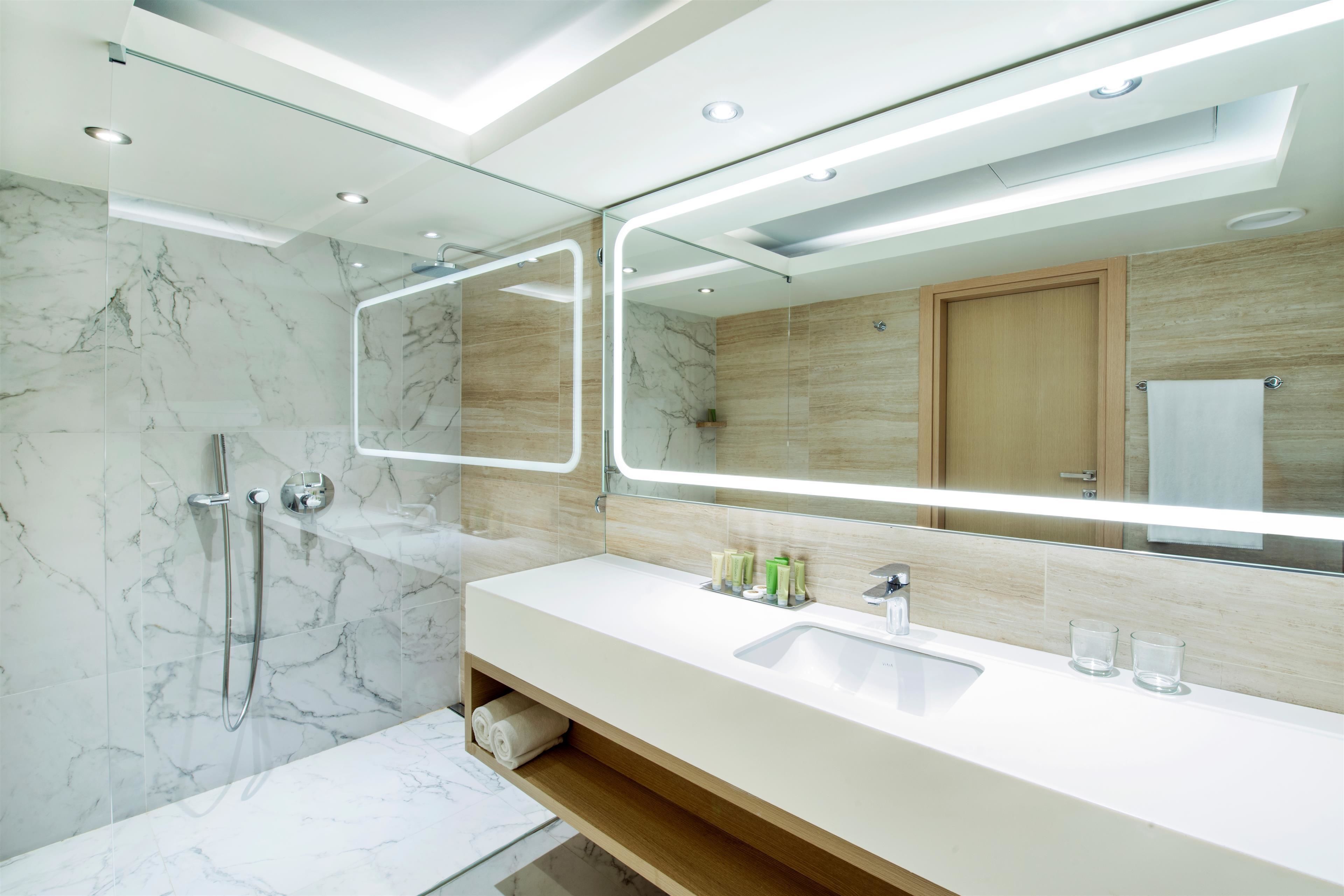 Un bagno moderno con doccia in marmo, uno specchio grande e un mobile lavabo in legno.