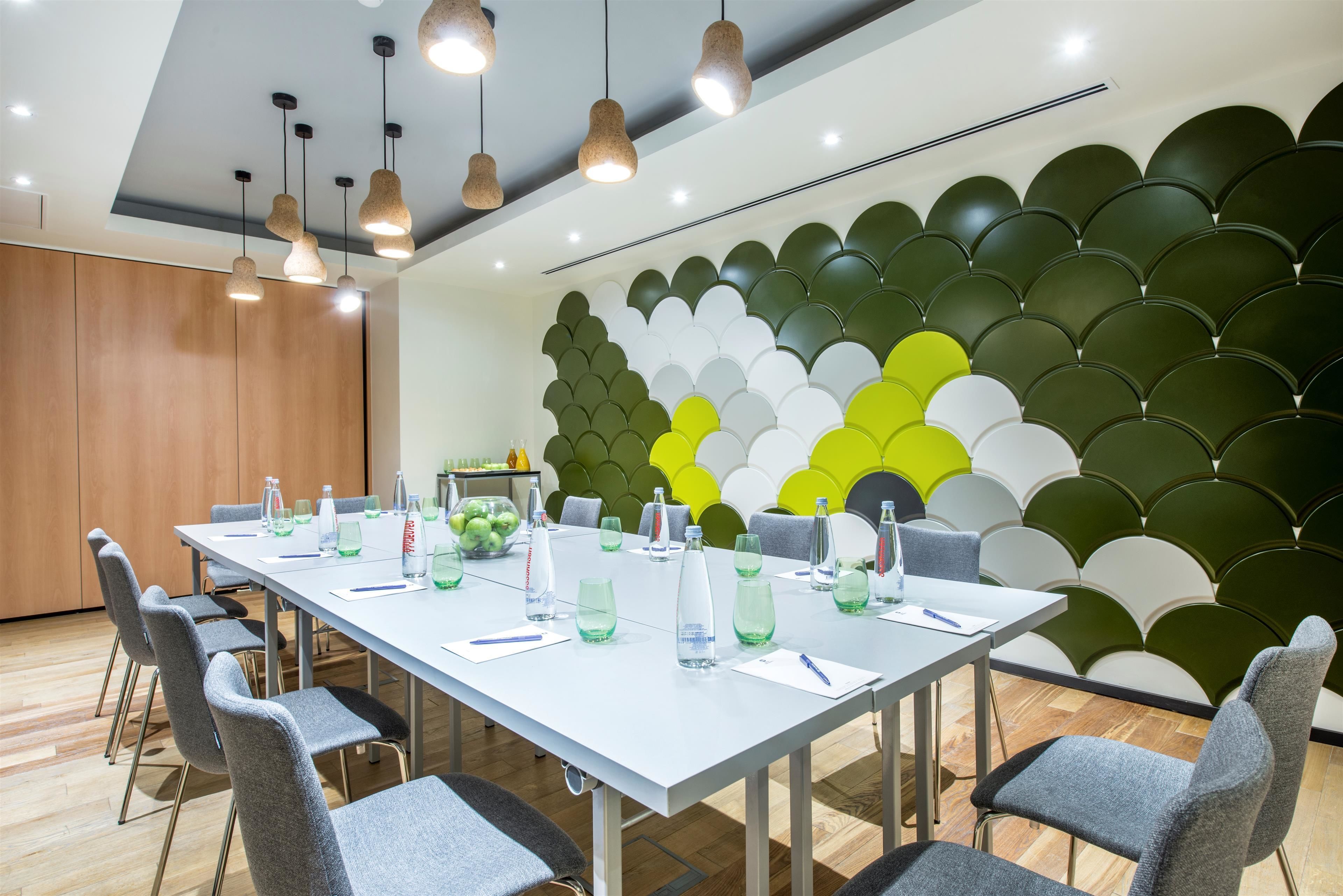 Ein Konferenzraum mit einem langen Tisch, grauen Stühlen und einem modernen Deckenstil.