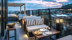 Una terraza en la azotea con mesa y sillas dispuestas, un sofá y vistas de la ciudad.