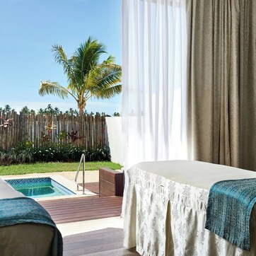 A spa room with a pool, a massage table, and a view of palm trees.