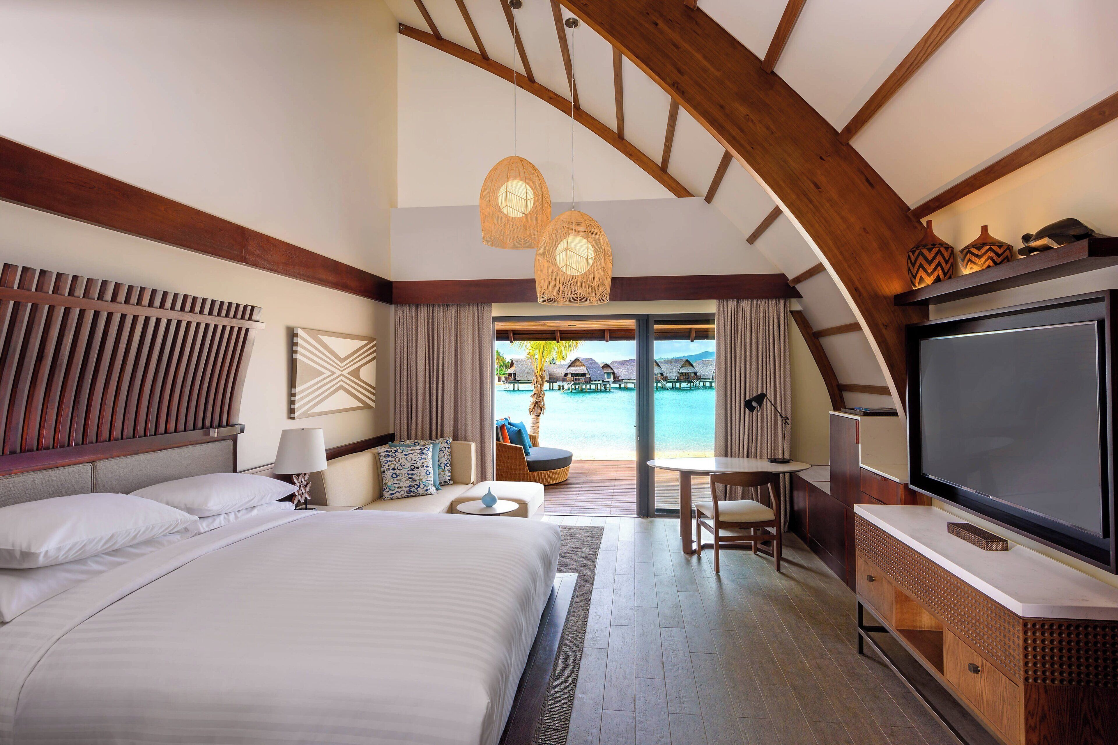 Habitación de hotel con una cama grande, televisión, escritorio y vista a una piscina.