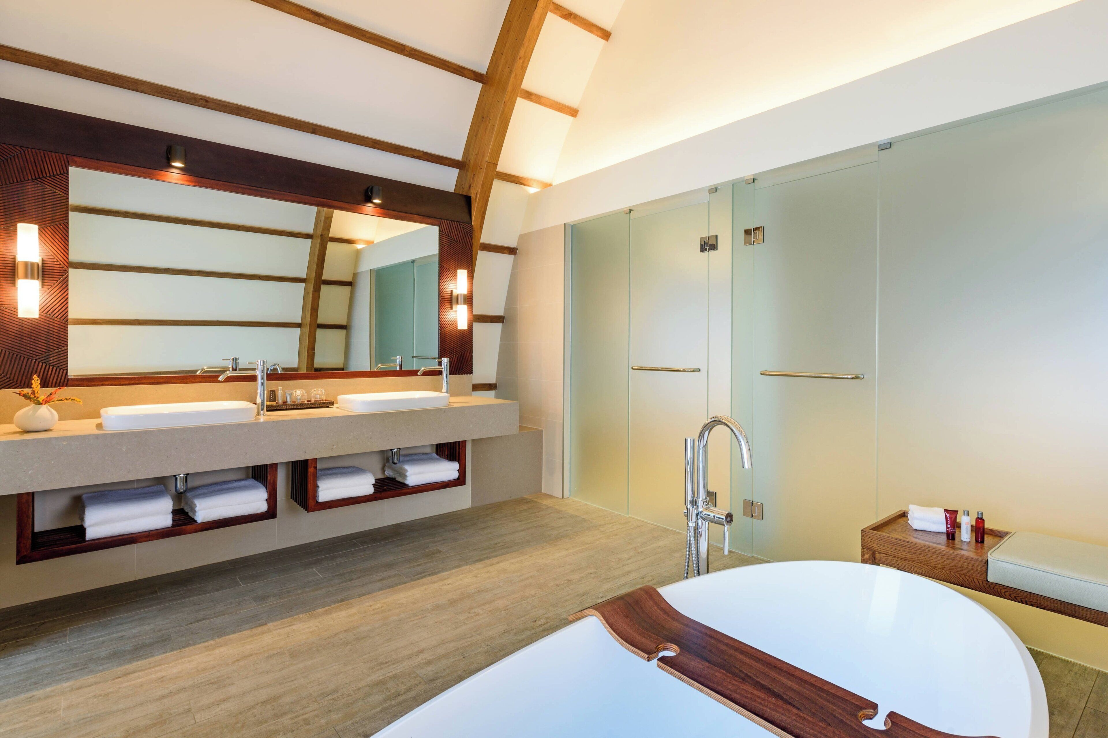 Un baño moderno con un espejo grande, dos lavamanos, una bañera y un box de ducha de cristal.