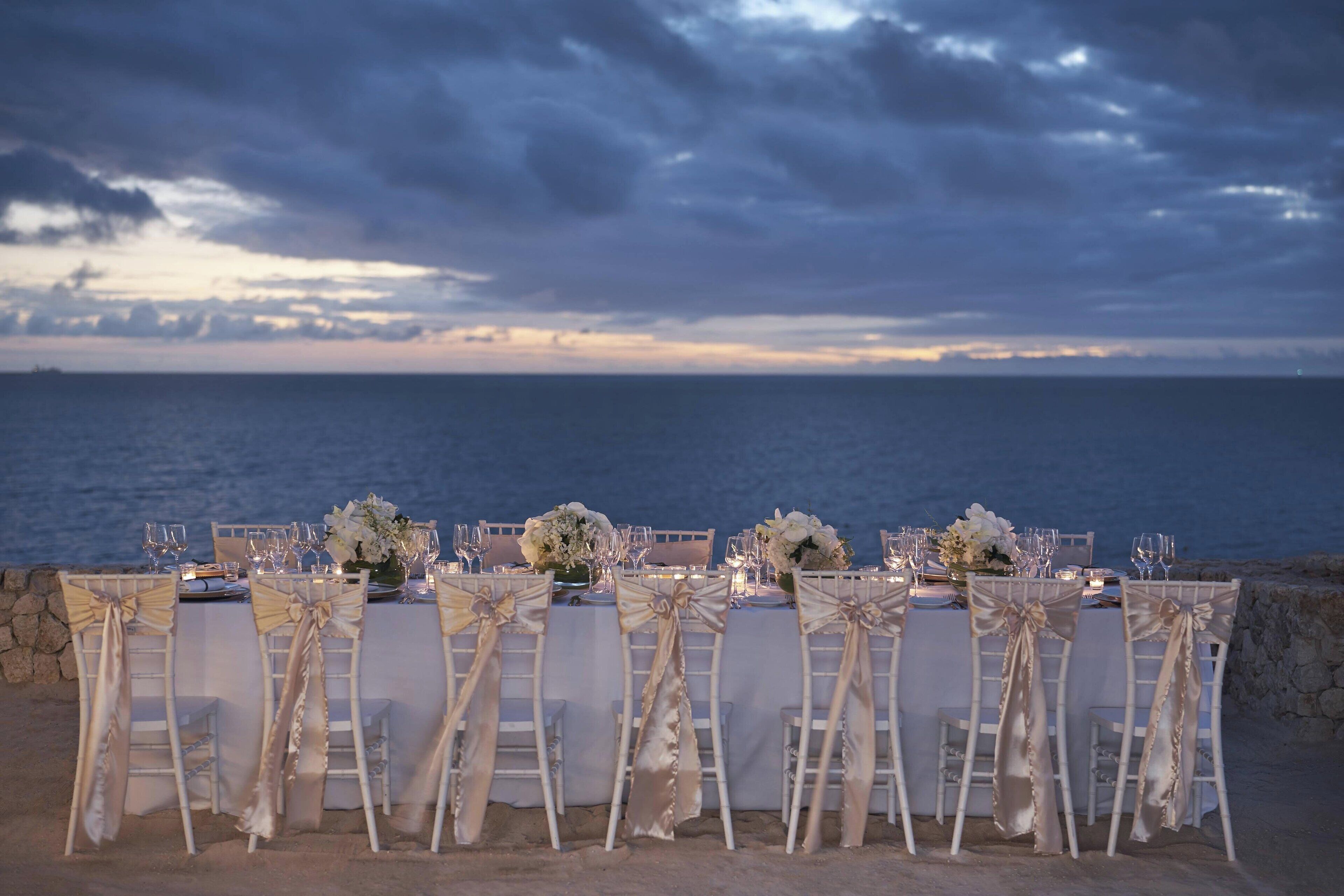 A seaside dining setup with white chairs and tables, overlooking the ocean.