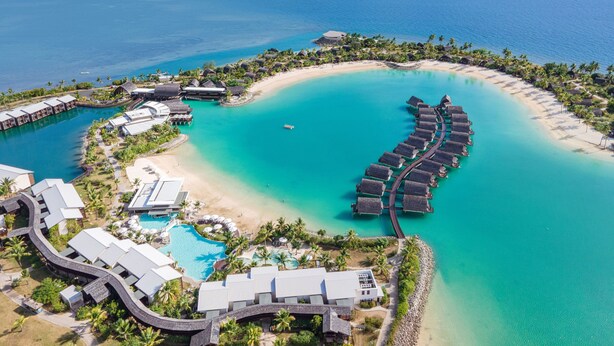 An aerial view of a resort with overwater bungalows, a beach, and a swimming pool.