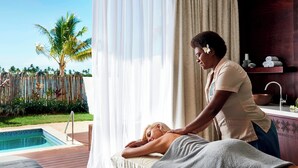 A person receiving a massage by a poolside with a view of palm trees and a wooden deck.