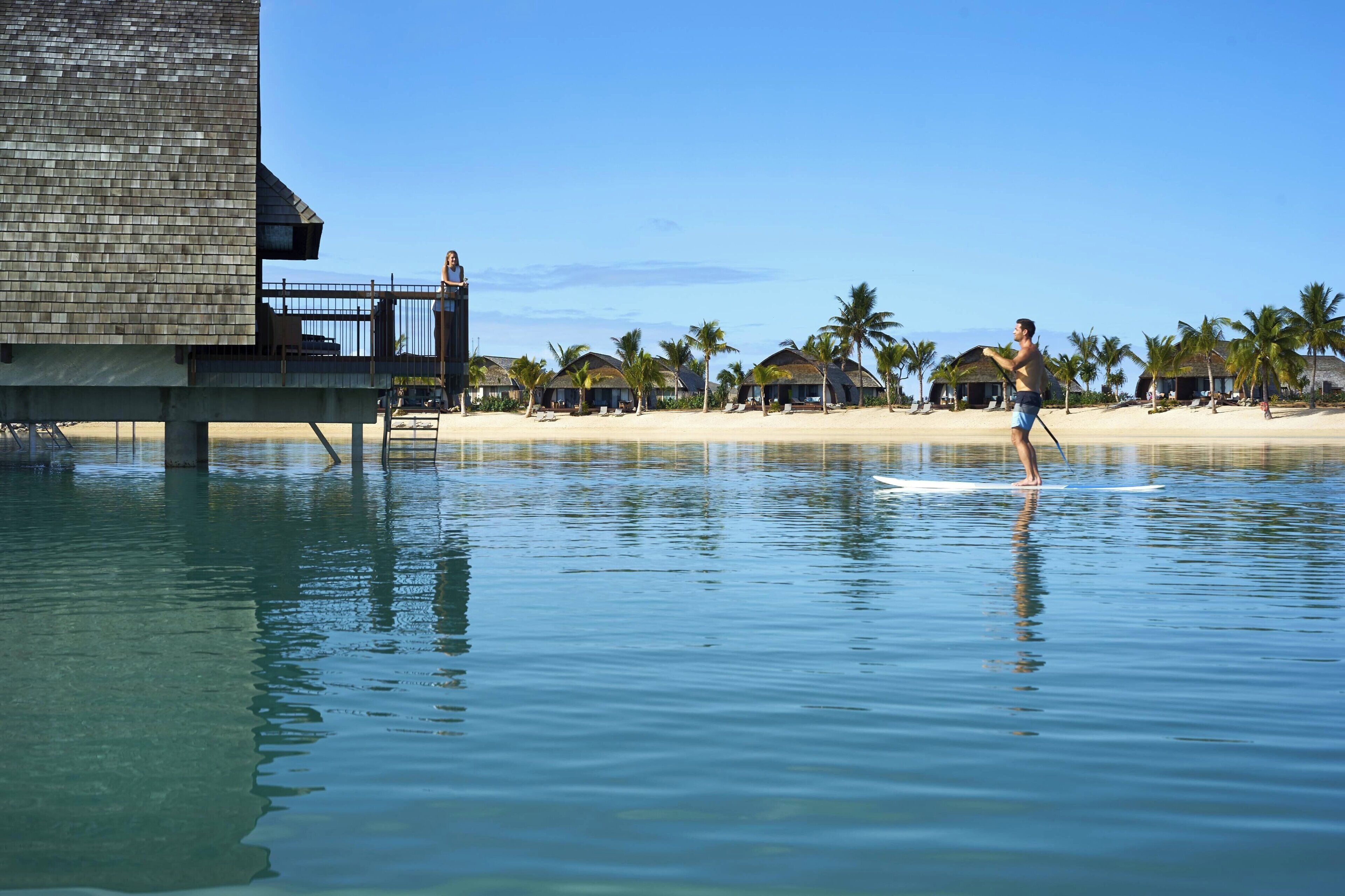 A beachfront property with overwater bungalows, a beach, and palm trees.