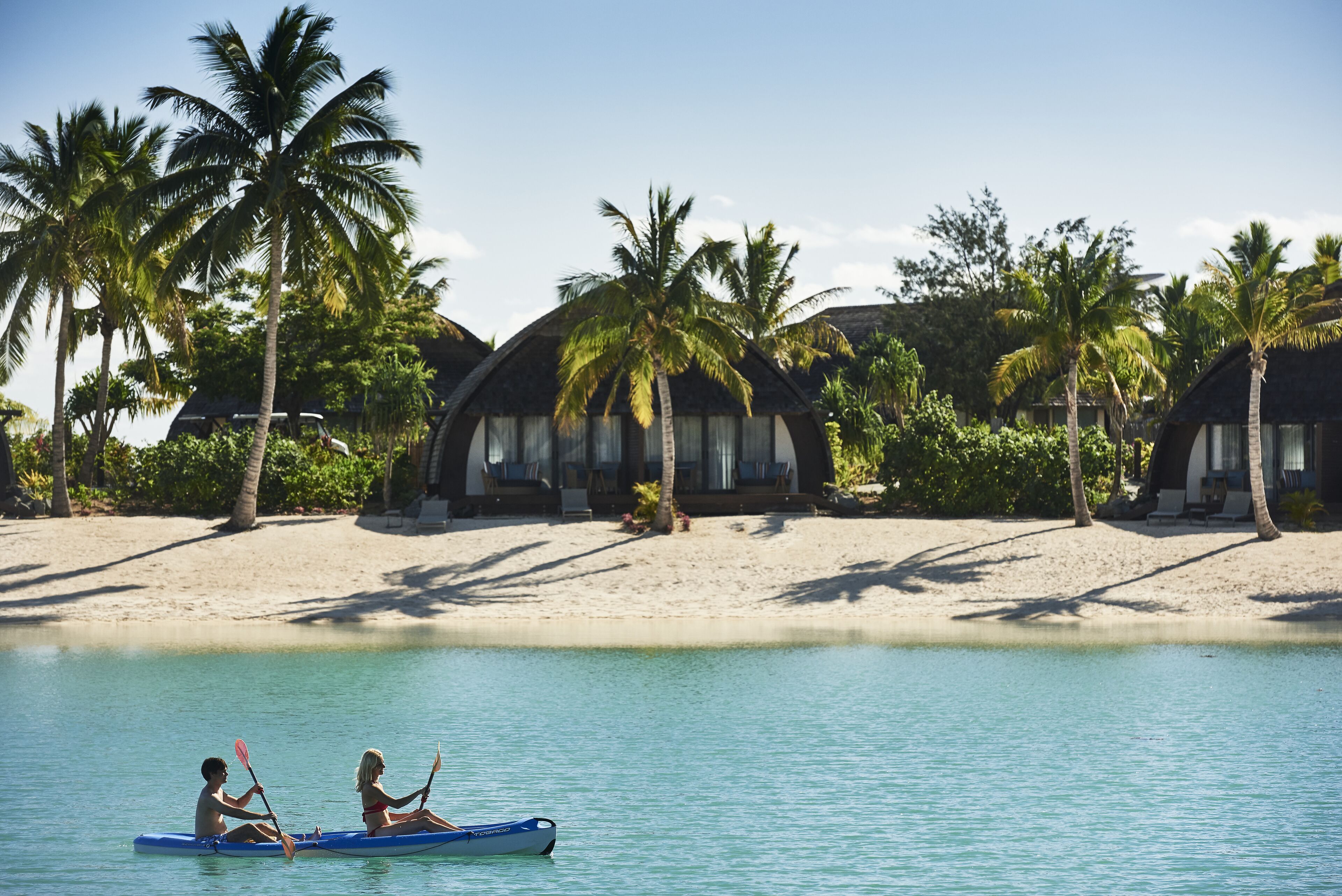 A beach with overwater bungalows, clear turquoise water, and palm trees.