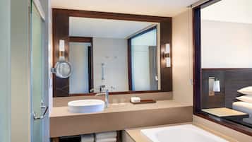 Un baño moderno con un espejo grande, un lavamanos redondo, una bañera y una cabina de ducha de vidrio.