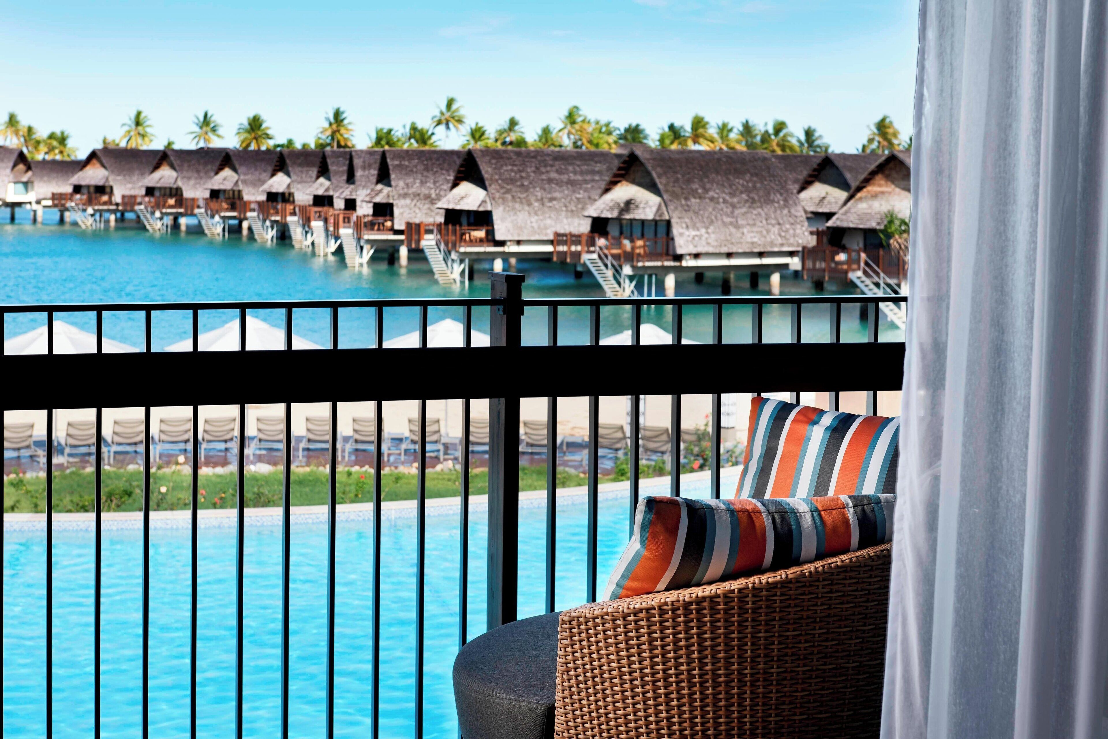 Ein Balkon mit Blick auf Bungalows über dem Wasser und einen Swimmingpool.