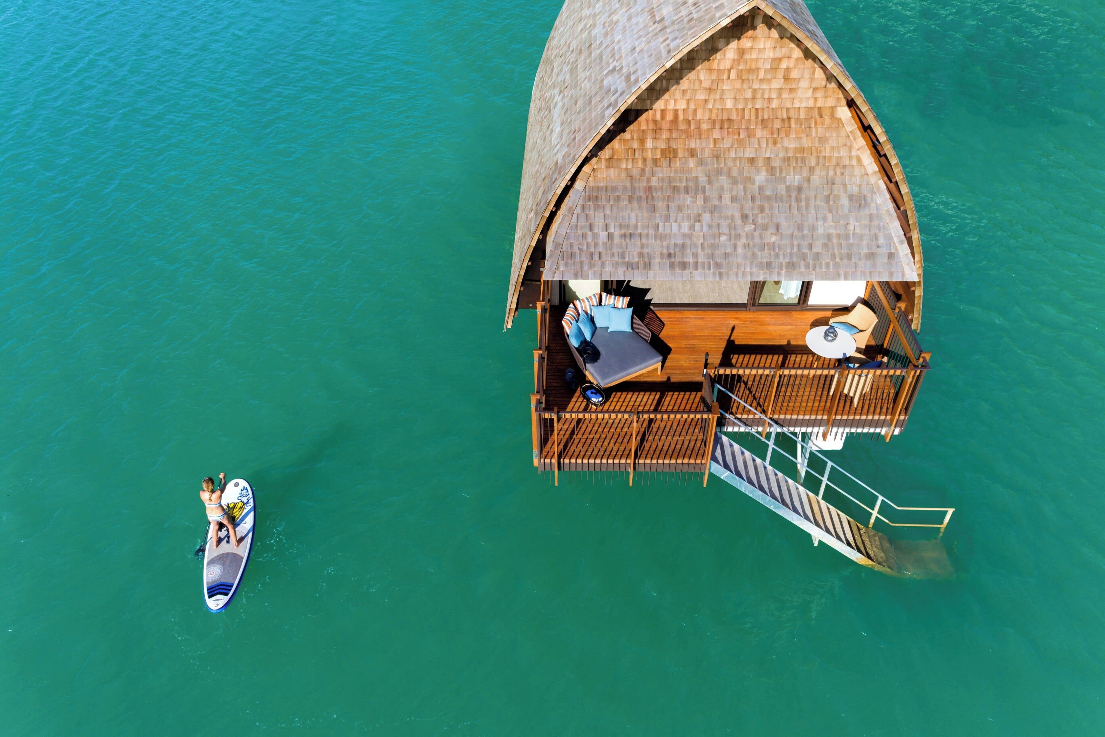 An overwater bungalow with a thatched roof, a wooden deck, and a small pool.