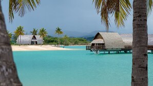 Waterbungalows met houten daken, een zandstrand en helder turquoise water.