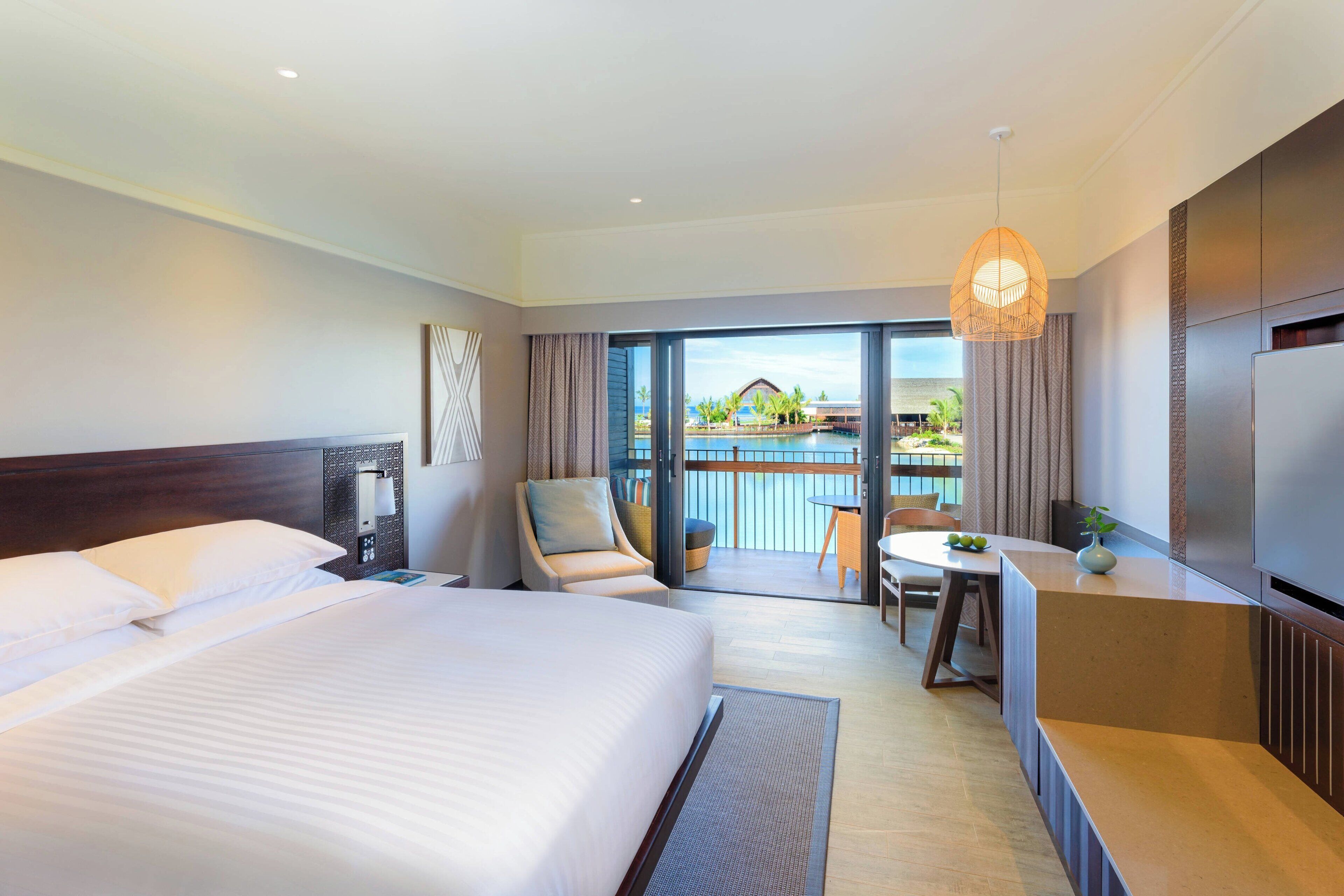 A hotel room with a large bed, a desk, a chair, and a view of a pool and building.