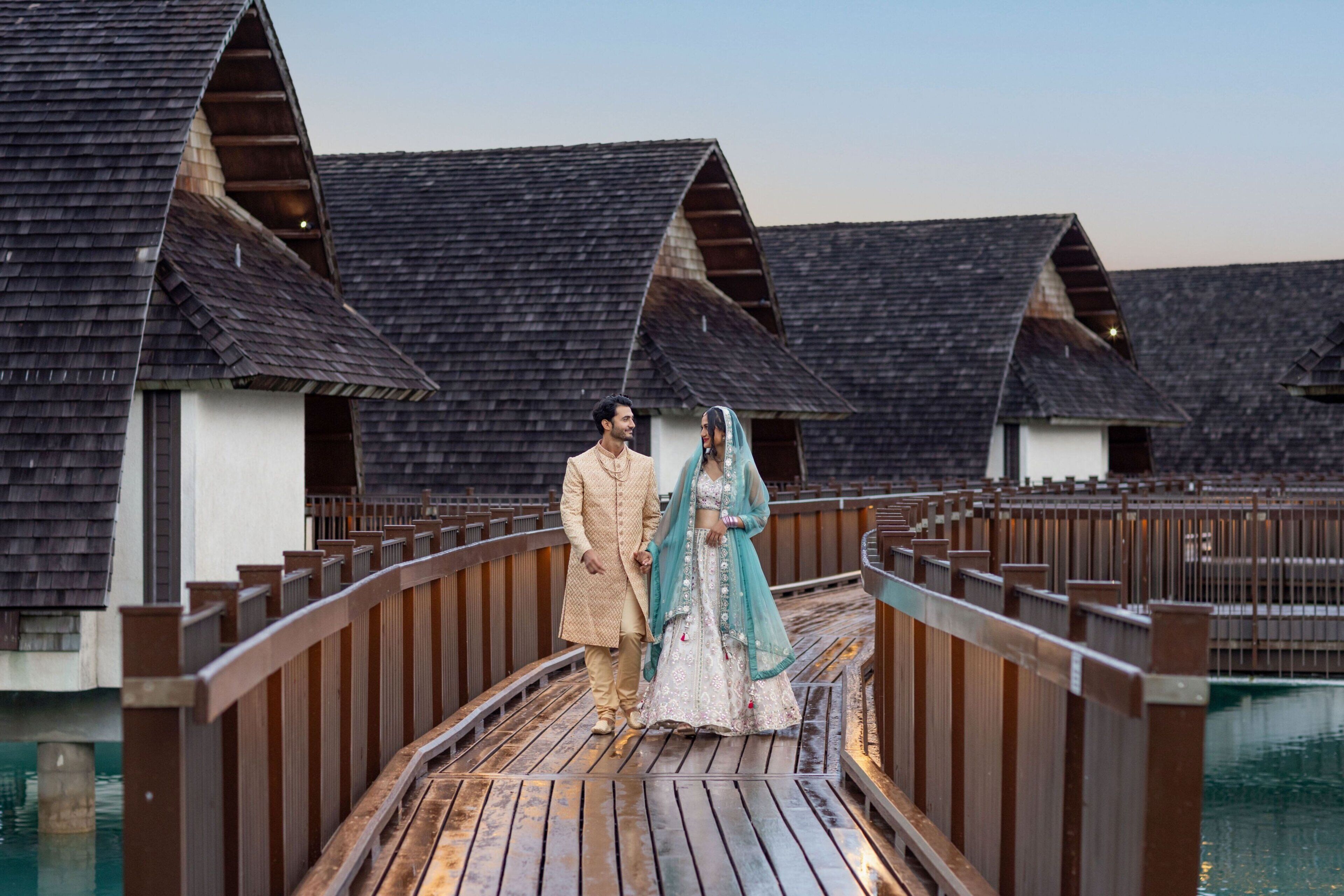 A wooden bridge connecting two overwater bungalows with a clear view of the water.