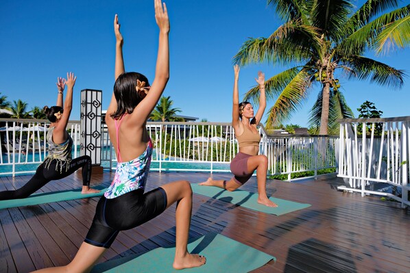 A group of people performing yoga on a wooden deck with a pool and palm trees in the background. - Fiji Marriott Resort Momi Bay (Momi)