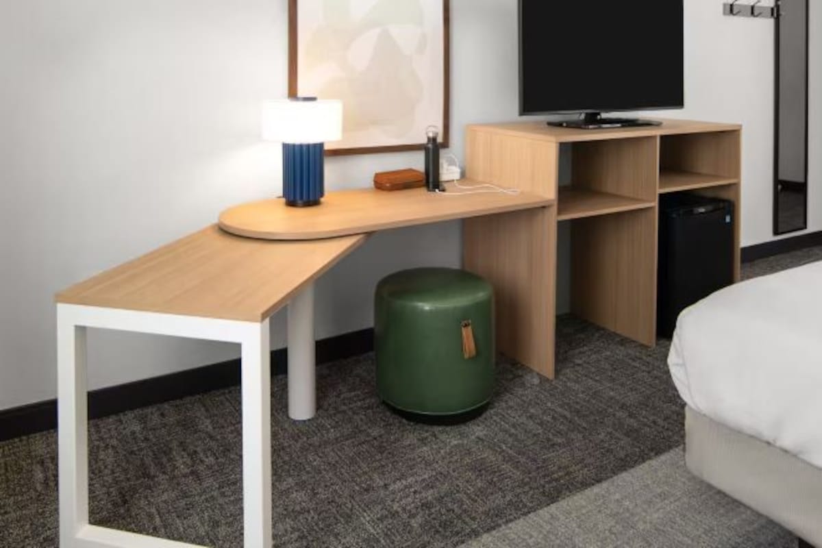 A hotel room with a wooden desk, a television, a green trash bin, and a bed.
