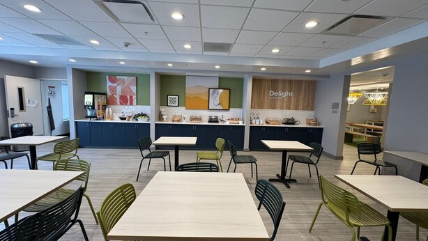 A modern cafe with multiple tables and chairs, a kitchen area, and a seating area with a view. - Spark by Hilton Erie (Erie)