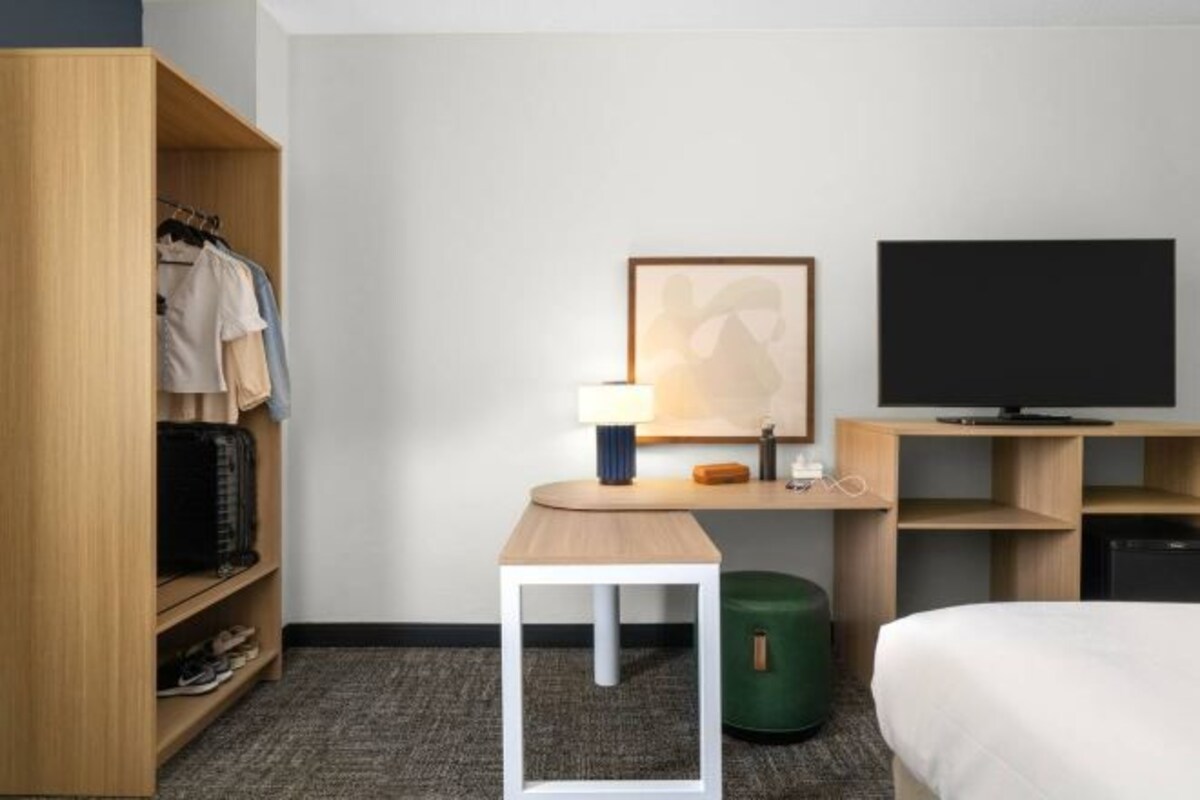 A hotel room with a bed, a desk with a lamp, a television, and a wardrobe.