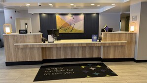 A hotel reception desk with a modern design, a large abstract painting above it, and a welcome mat with a message. - Spark by Hilton Erie (Erie)