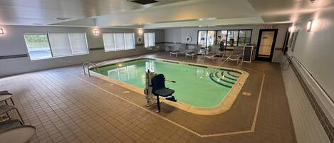 An indoor swimming pool with clear lane markings, a lifeguard chair, and lounge chairs around the pool area.