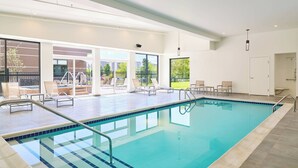 A modern indoor swimming pool with clear blue water, a tiled deck, and a glass-enclosed patio area with lounge chairs. - Element by Marriott West Des Moines (West Des Moines)