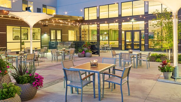 An outdoor patio area with tables and chairs, string lights, and potted plants. - Element by Marriott West Des Moines (West Des Moines)