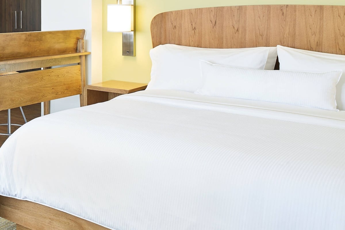 A neatly made bed with white linens, a wooden headboard, and a bedside table with a lamp.